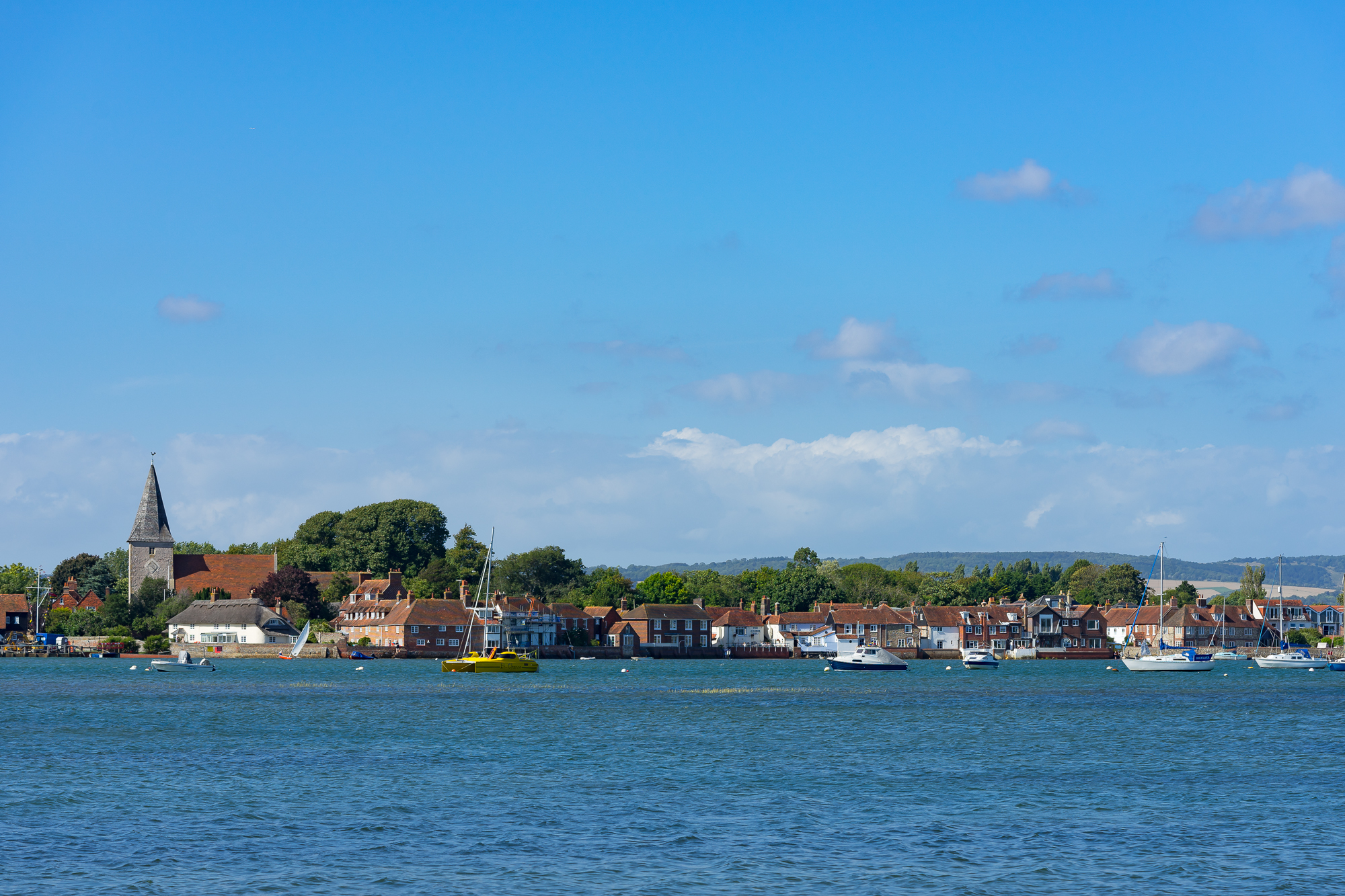 Bosham across the water on a blue day: the church spire, moored boats and the waterfront