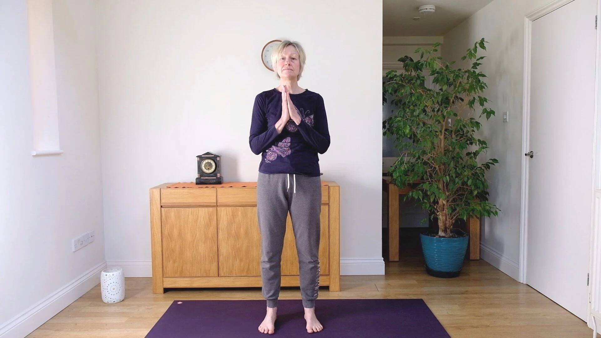 Viv standing in prayer position on a purple mat in a plain room